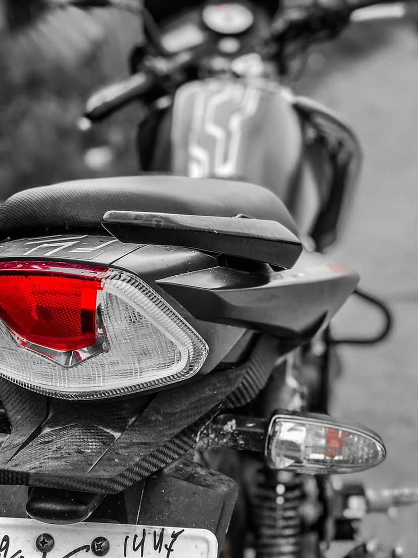Red motorcycle tail light illuminated against a monochrome rear fender showing carbon fiber and metal parts.