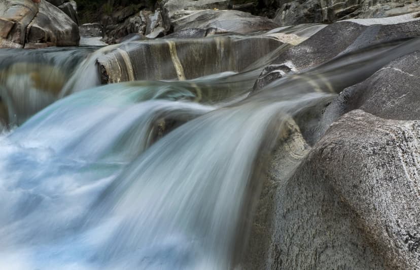 Silky white water ribbons flow over smooth grey granite rocks in a tranquil long-exposure river landscape.