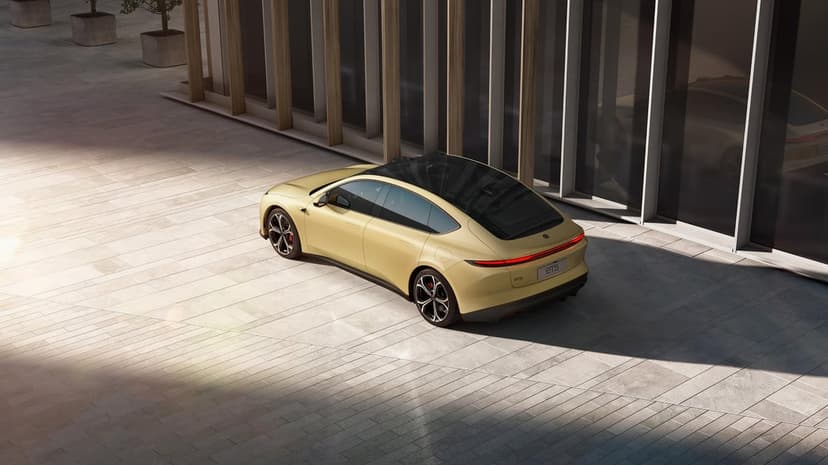 Rear view of a gold electric NIO ET5 sedan parked on stone tiles beside a modern glass and wood building.