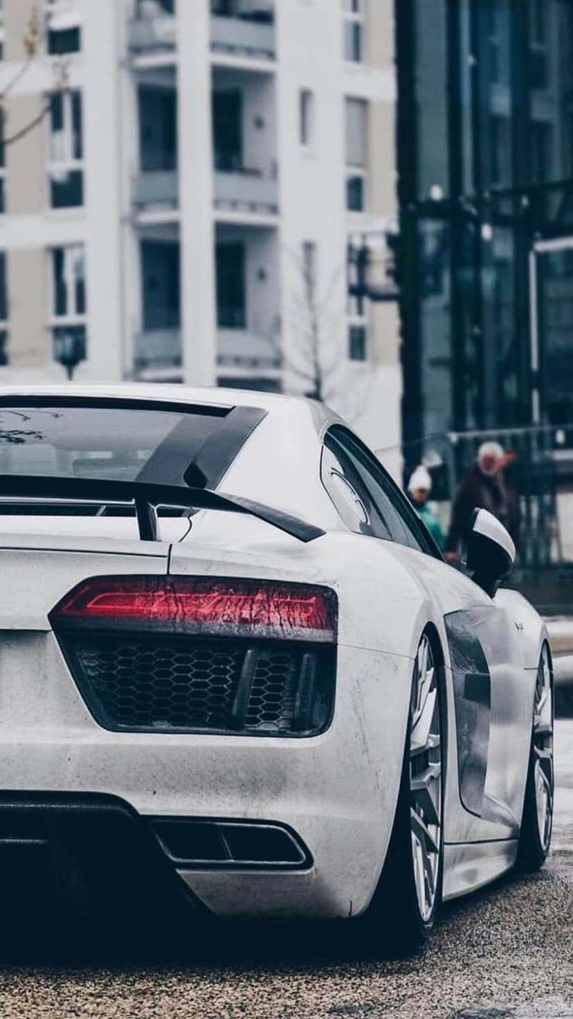 White Audi R8 supercar rear view featuring red LED taillights and a spoiler on a damp urban street after rain.