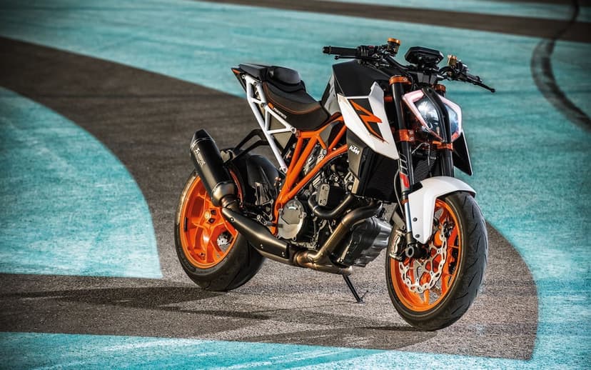 KTM 1290 Super Duke R motorcycle with orange frame and wheels on a blue and grey paved track surface.