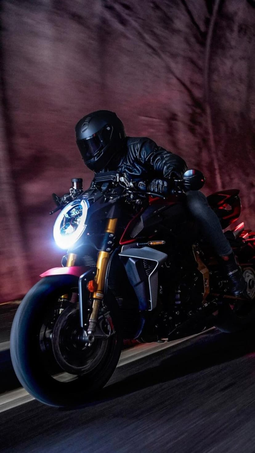 Motorcyclist in black leather riding a sportbike through a dark tunnel with a bright white headlight beam.