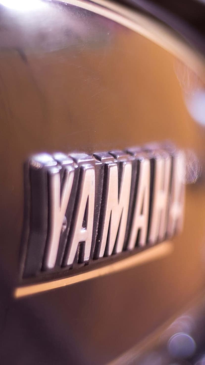 Yamaha chrome emblem with polished metallic lettering reflecting light on a dark textured motorcycle surface.