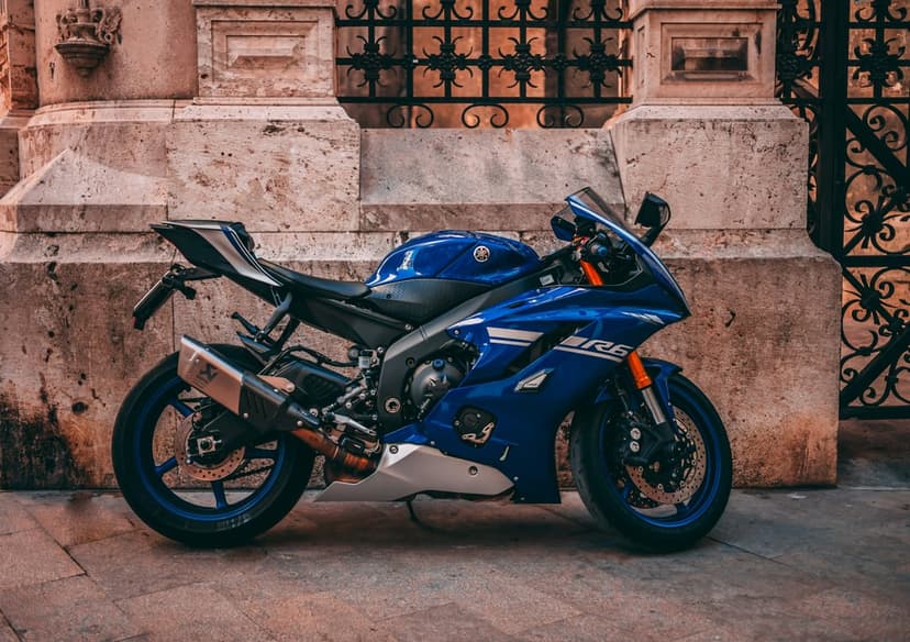 Blue Yamaha R6 motorcycle parked on a paved street beside an ornate stone building with decorative ironwork.