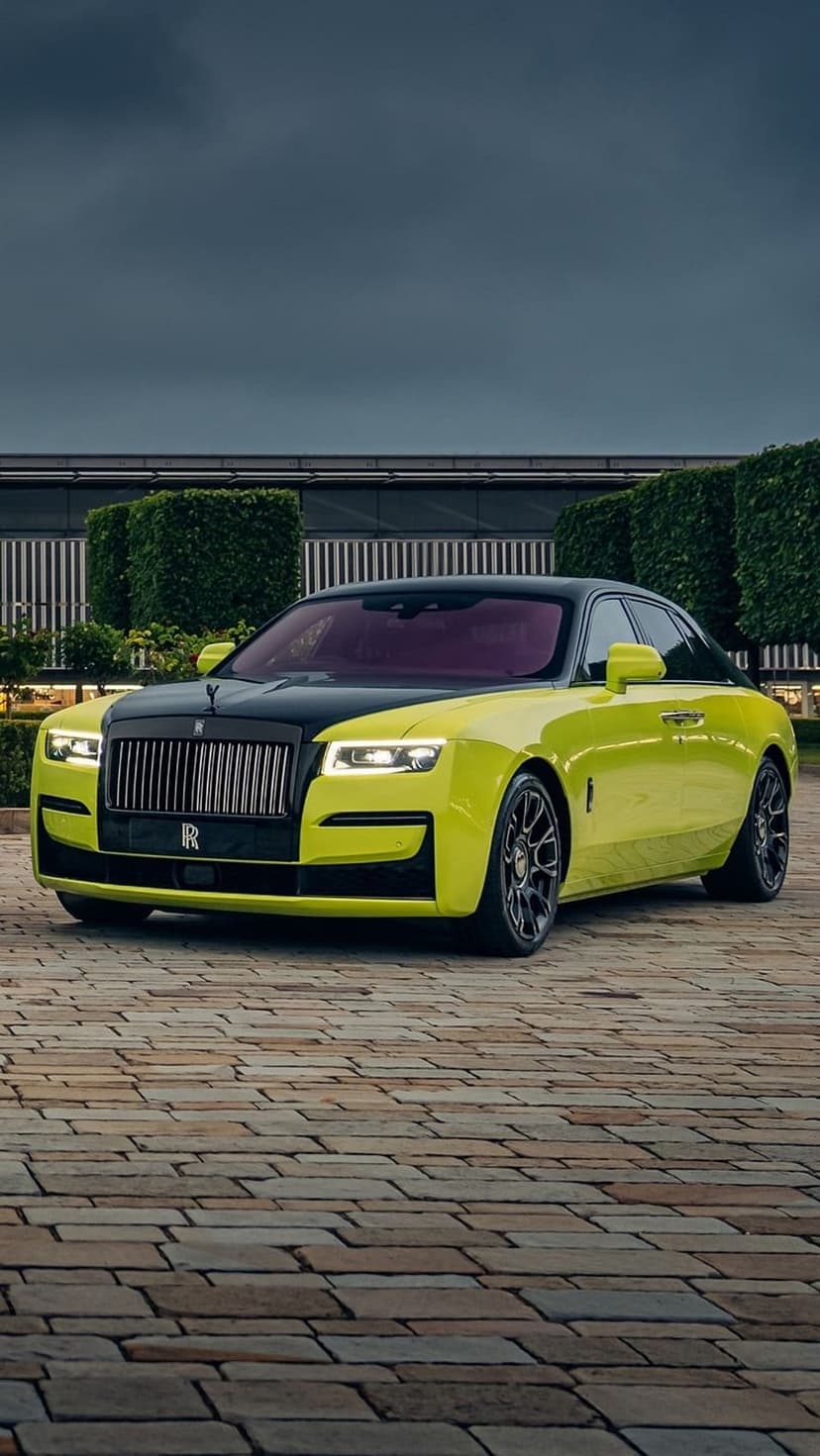 Lime green Rolls-Royce Ghost with a black hood parked on a stone driveway in front of a modern house.