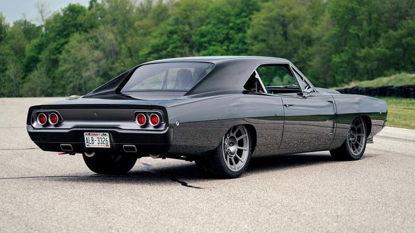 Black custom 1968 Dodge Charger muscle car with lowered stance and grey wheels on a grey asphalt track.