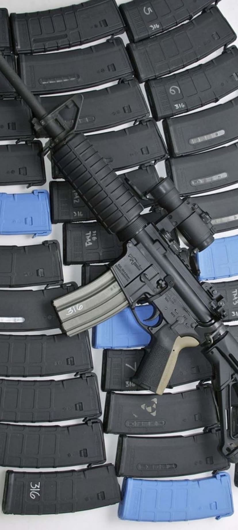 Black AR-15 rifle with optical sight surrounded by neatly organized blue and black ammunition magazines.