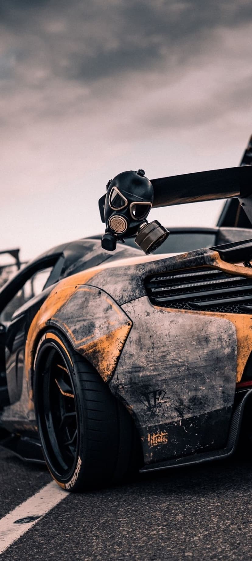 Weathered McLaren supercar with a gas mask mounted on its rear wing under a dark, overcast dystopian sky.