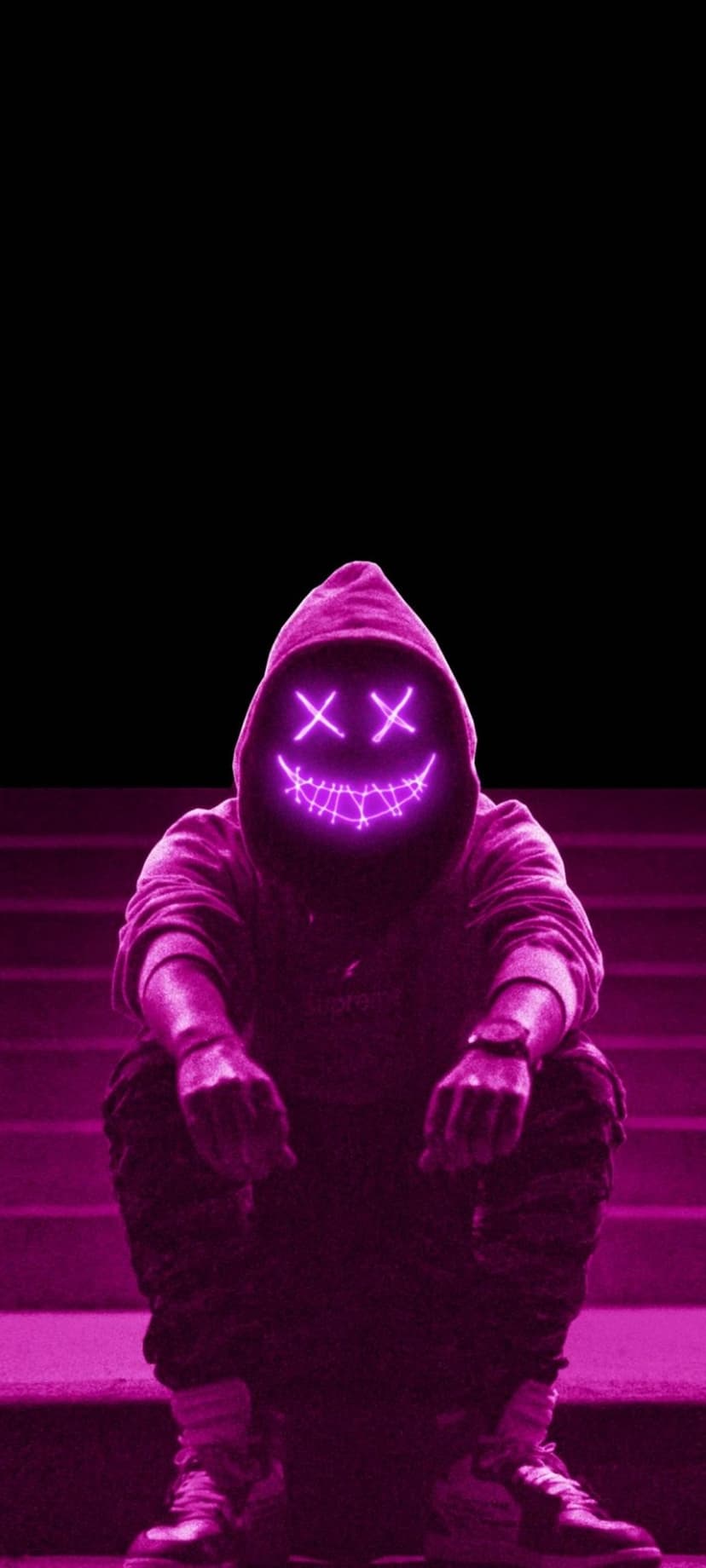 Person in a black hoodie wearing a glowing neon pink cross-eye mask while sitting on shadowy concrete stairs.