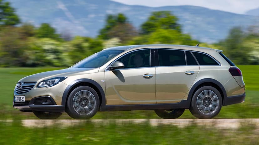 Gold Opel Insignia Country Tourer wagon speeding past green fields and mountains with motion blurred wheels.