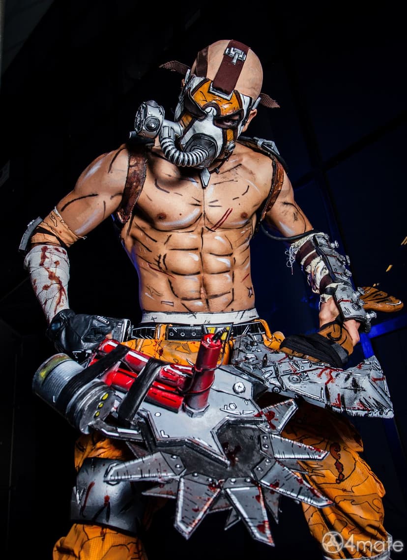 Man in Krieg Borderlands cosplay wearing a gas mask and holding a blood-stained buzz axe in a dark studio setting.