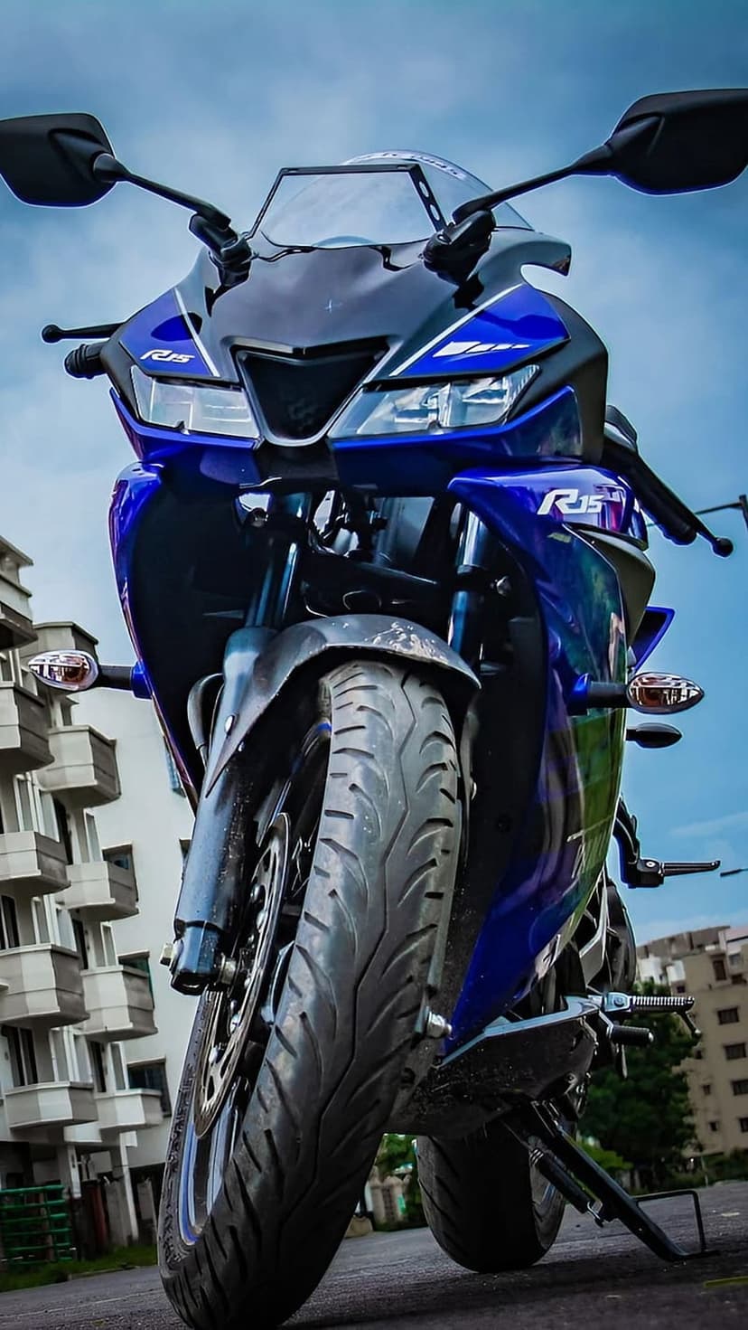 Yamaha R15 V3 sportbike in blue features aggressive headlights and sharp fairings against a cloudy sky background.