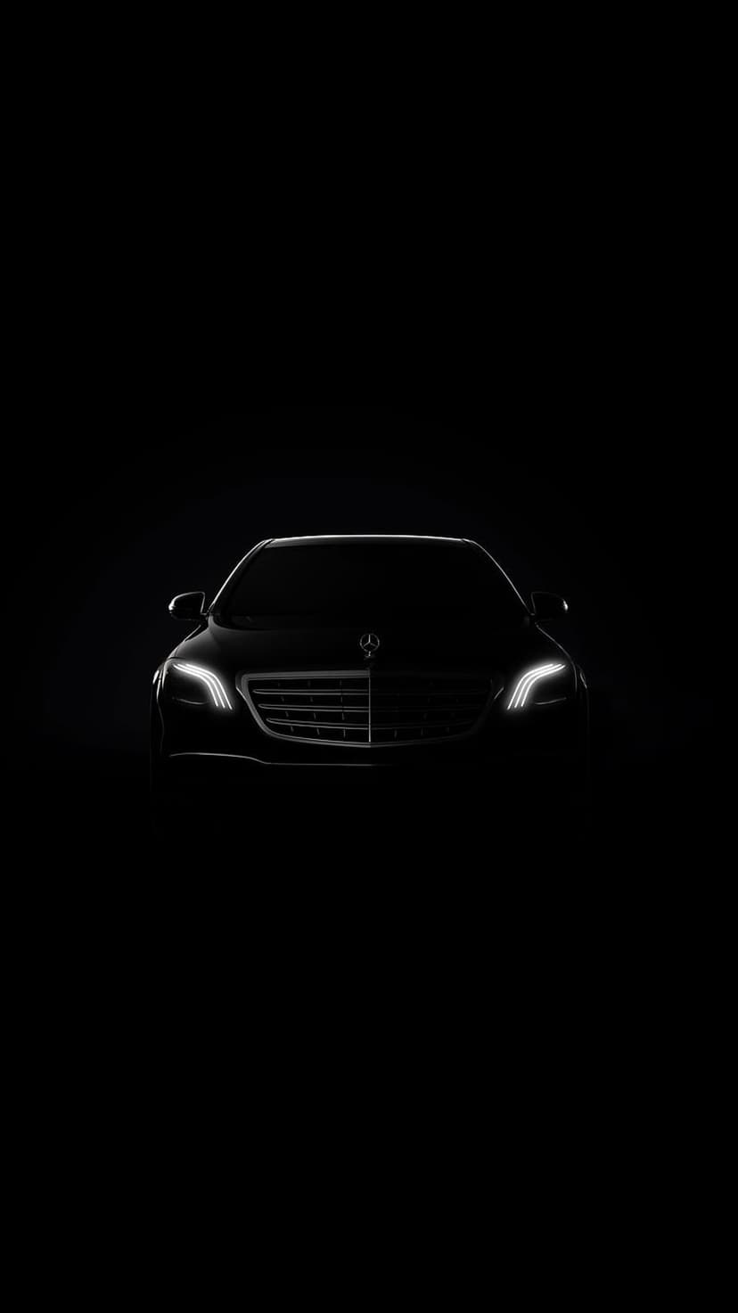 Mercedes-Benz sedan with glowing LED headlights and a chrome grille emerging from a dark black background.