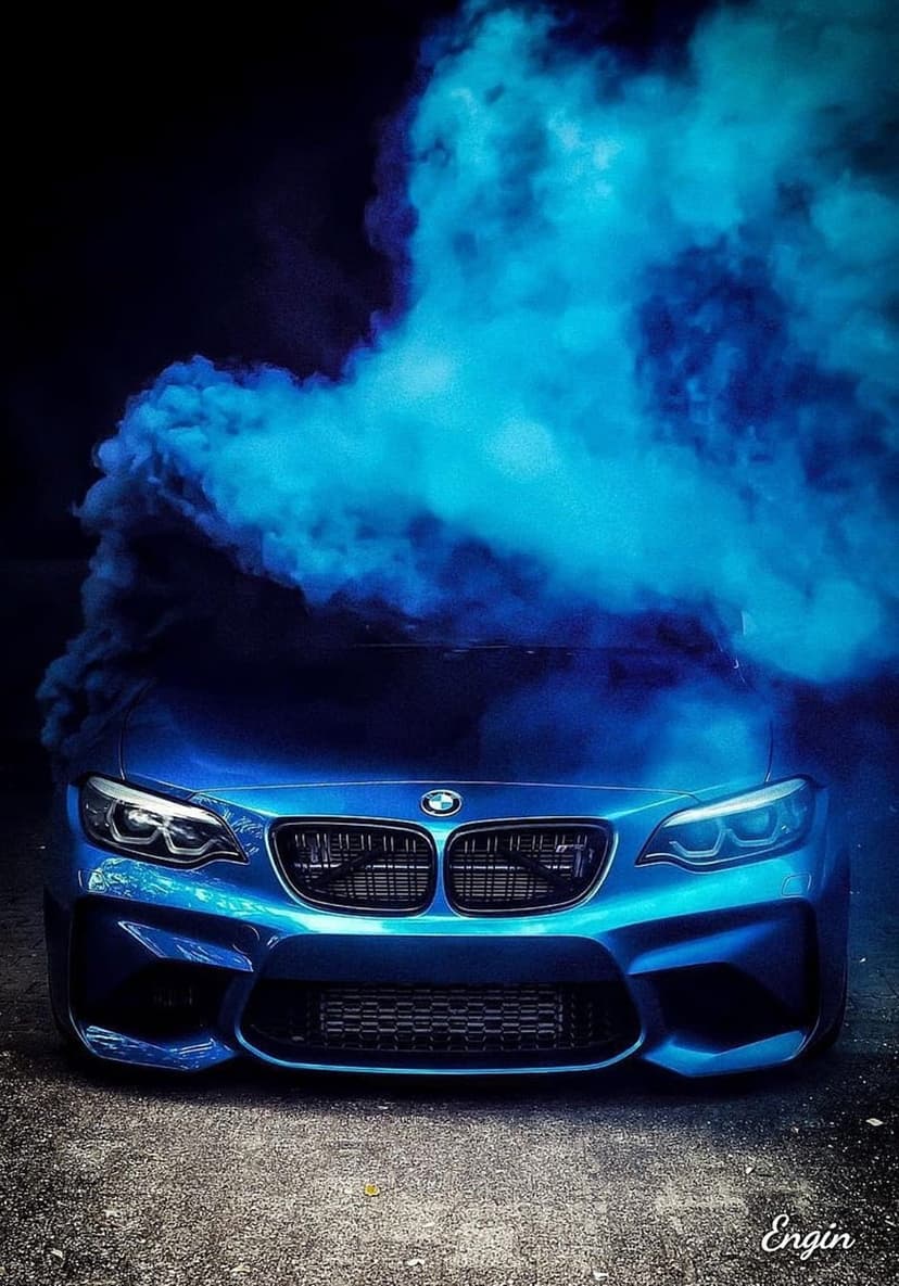 Blue BMW M2 sports car with illuminated headlights surrounded by dense clouds of swirling azure smoke.