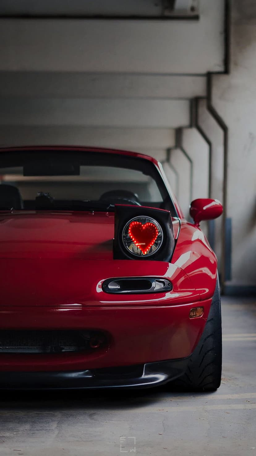 Crimson Mazda Miata featuring a glowing heart-shaped pop-up headlight modification inside a concrete structure.
