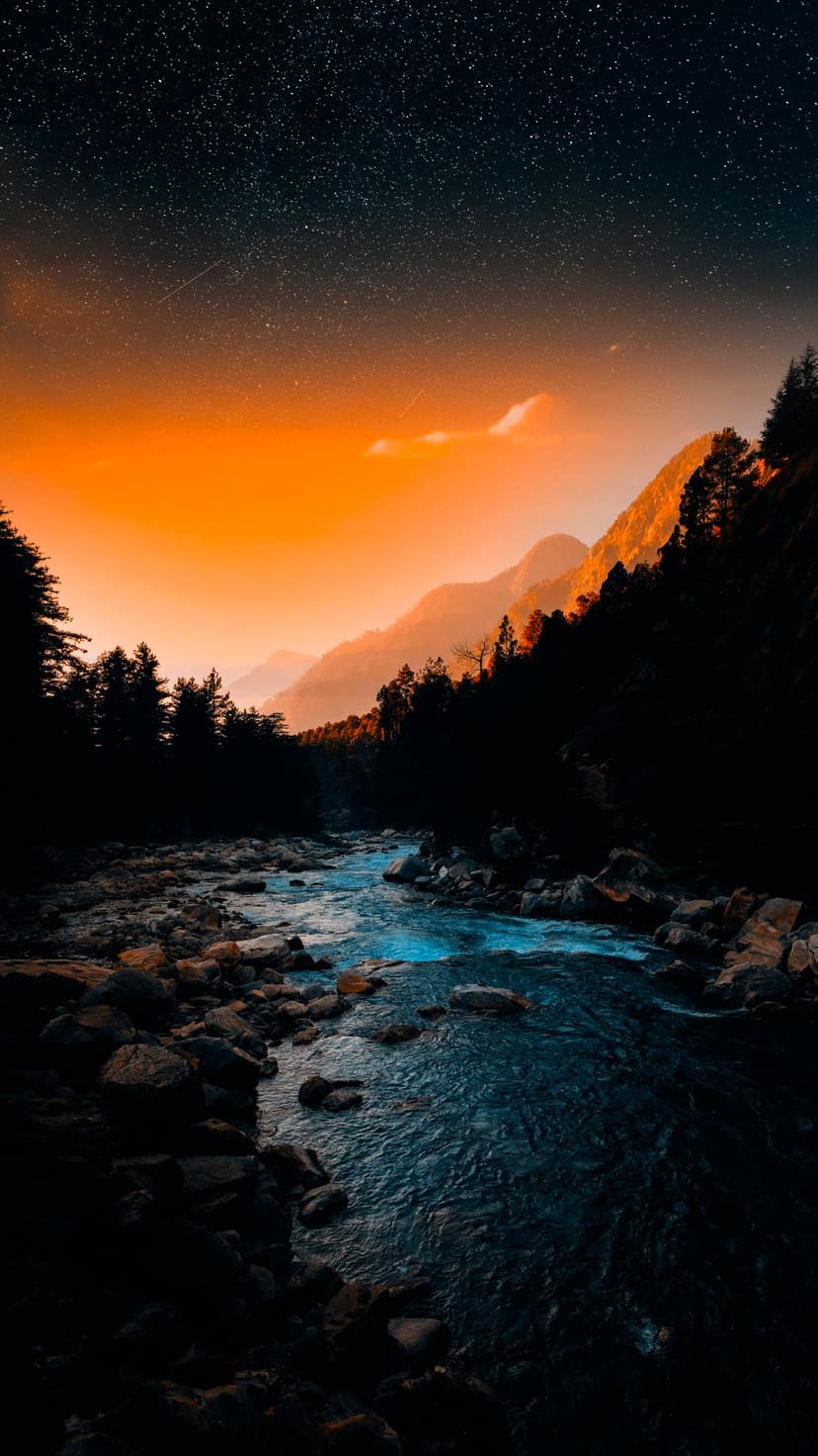 Rocky river flows through a dark forest under a transition sky featuring bright orange light and distant stars.