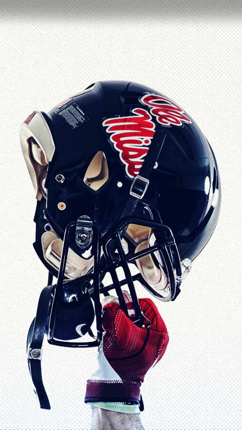 Football helmet with a red swirl design held by a person in a red glove against a textured light grey background.