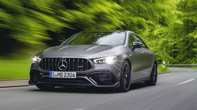 Matte gray Mercedes-AMG CLA sedan driving fast on a curved road with green motion blur and glowing headlights.