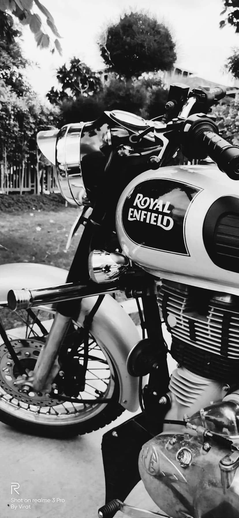 Royal Enfield motorcycle fuel tank and chrome engine details in a monochrome close-up with dappled sunlight.