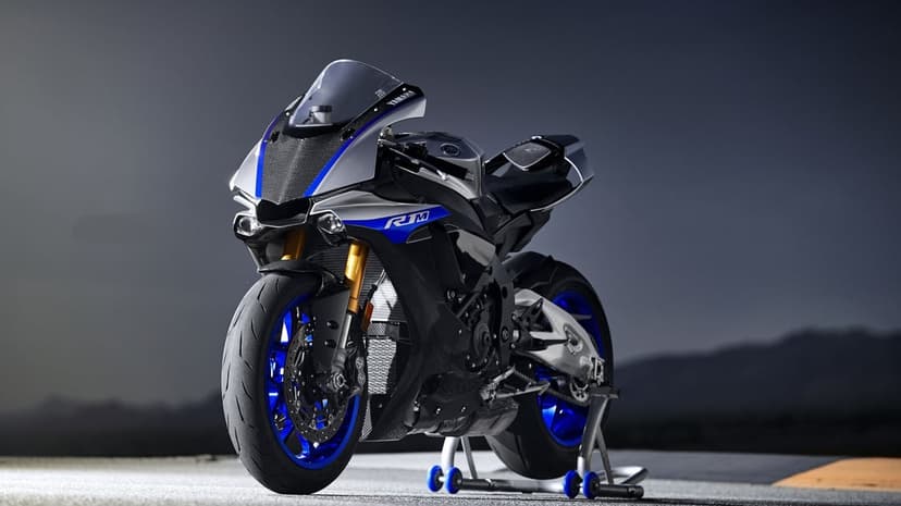 Yamaha R1M sportbike with carbon fiber fairings and blue wheels on a paddock stand under dramatic studio light.