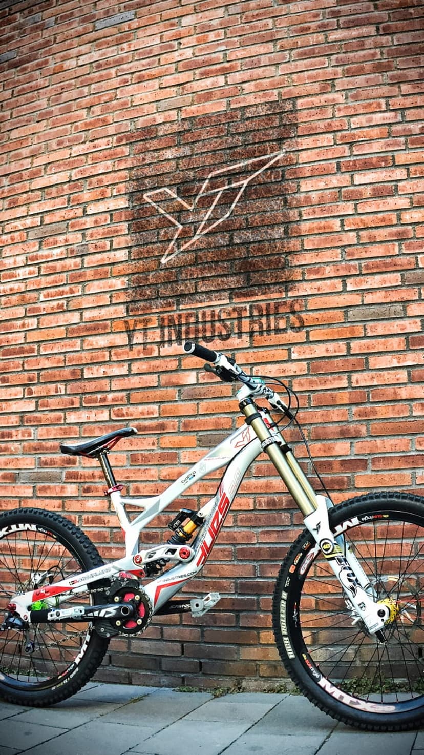 White and red YT Industries downhill mountain bike leaning against a textured red brick wall in portrait view.