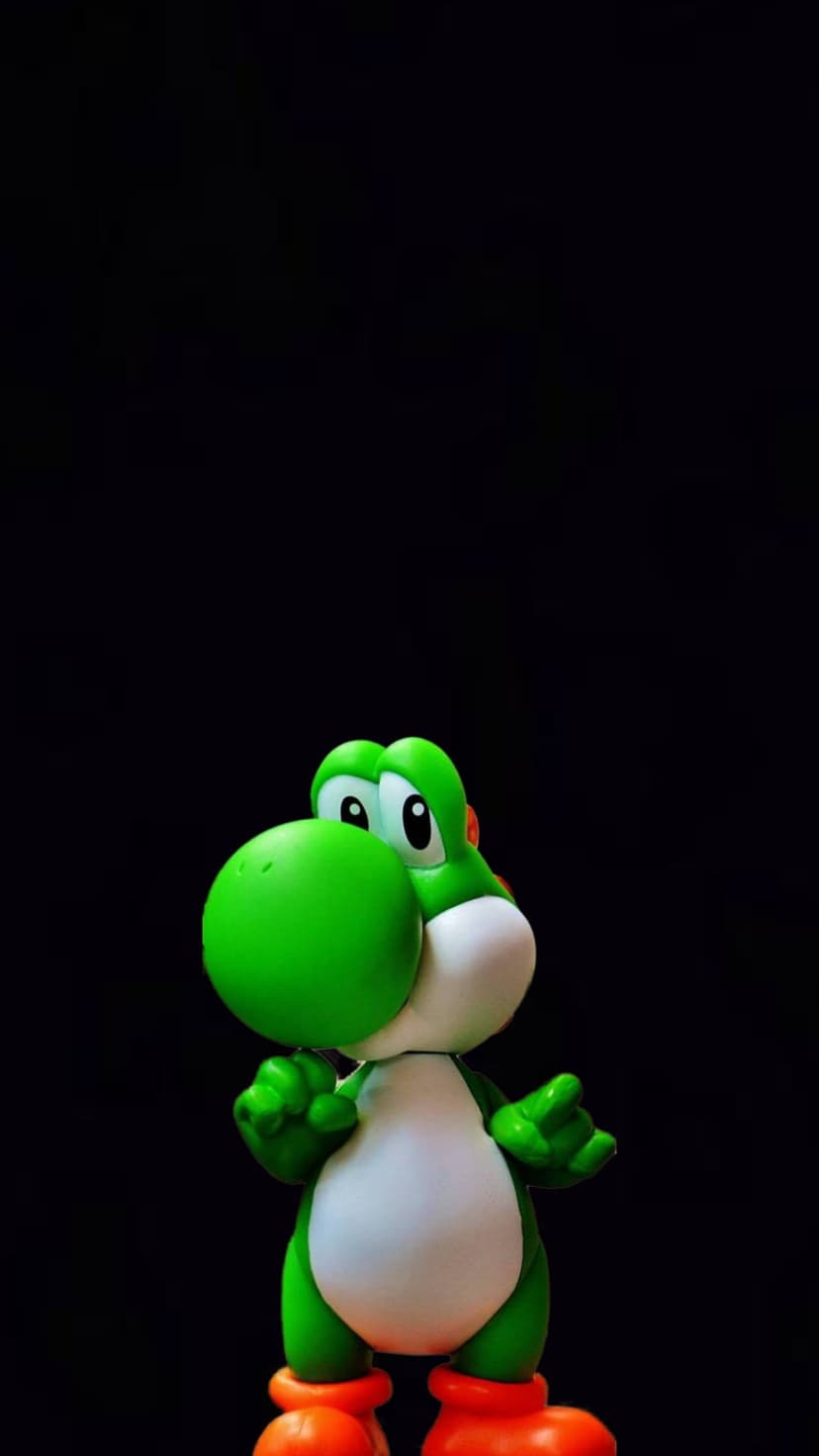 Green Yoshi toy with orange boots and white belly posing against a solid black backdrop in sharp studio lighting.
