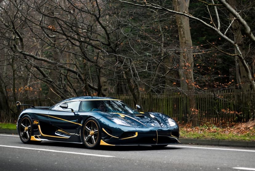 Blue and gold Koenigsegg Agera RS hypercar parked on an asphalt road surrounded by bare winter trees.