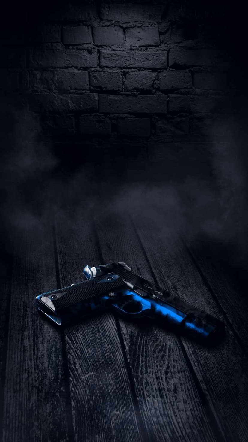 Camouflage handgun in blue and black resting on rustic timber with atmospheric smoke and a dark brick wall.