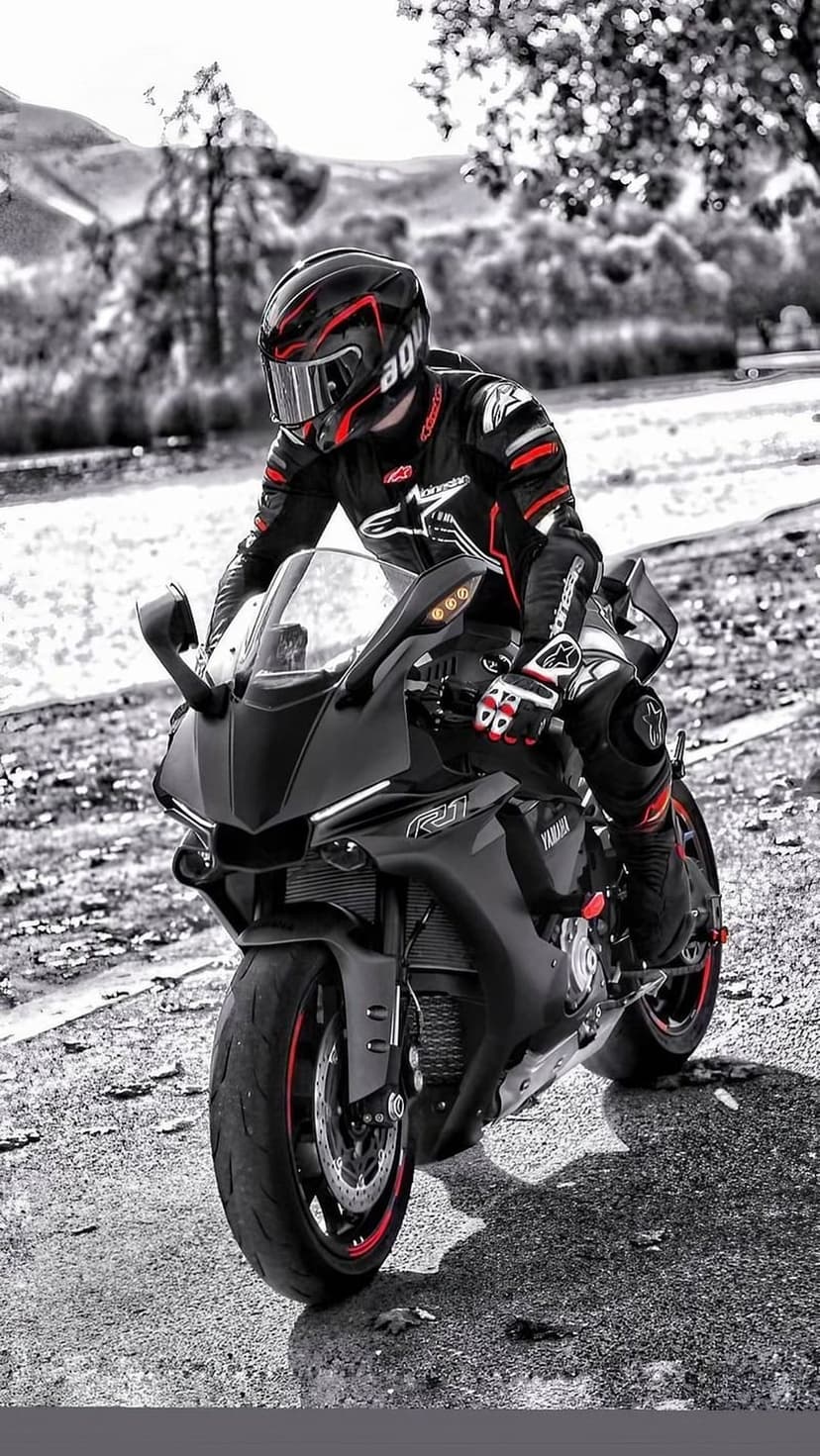 Motorcycle rider in a black and red suit on a Yamaha R1 racing bike along a dusty gravel road.