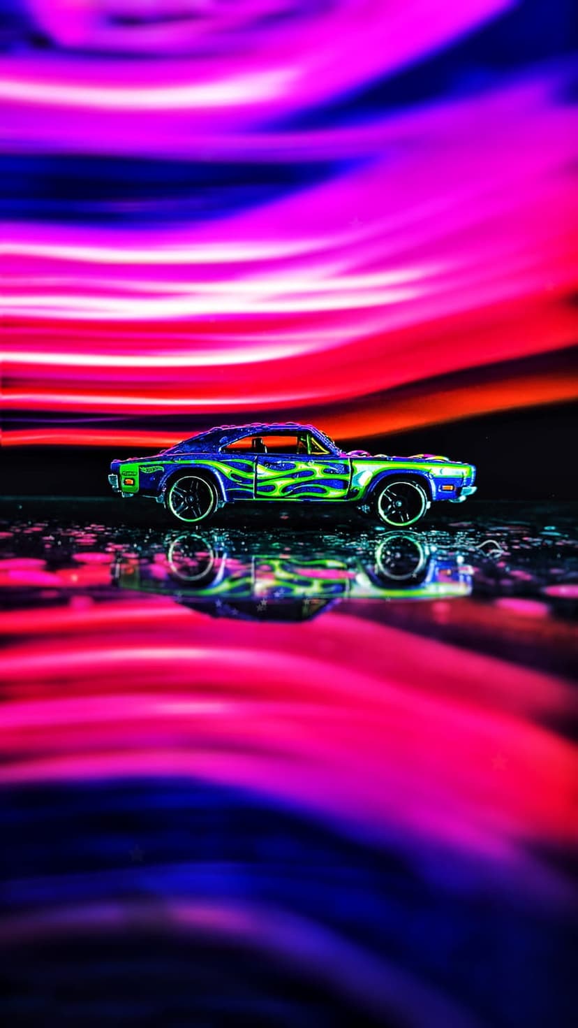 Blue toy car with green flames on a wet surface reflecting pink and purple neon light streaks in the dark.