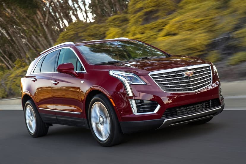 Deep red Cadillac SUV driving fast on a forest road with motion blurred wheels and trees in the background
