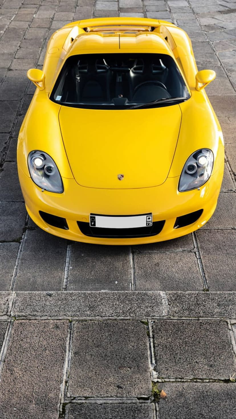 Yellow Porsche Carrera GT supercar parked on a cobblestone street captured from a high overhead perspective.