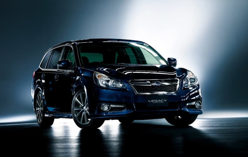 Dark blue Subaru Legacy Touring Wagon with rim lighting and silver wheels against a moody studio background.