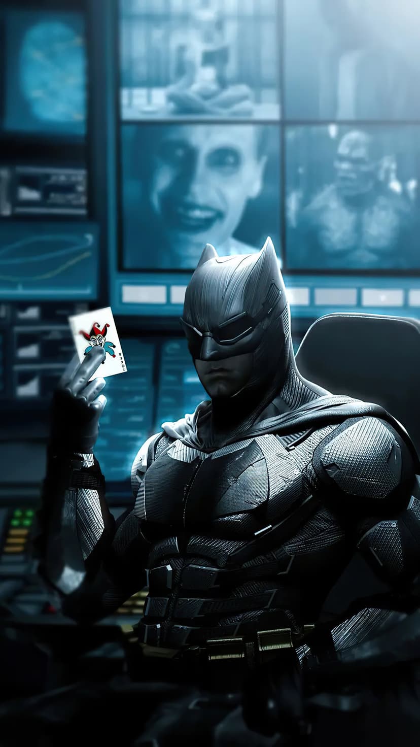 Batman in tactical armor holds a Joker card before glowing blue computer monitors in a dark high-tech cave.