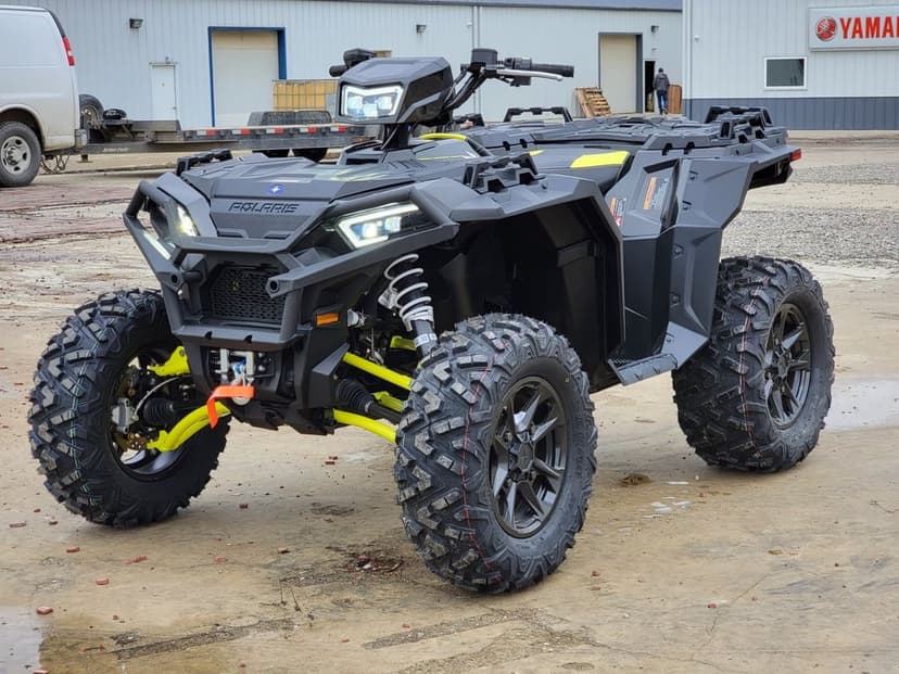 Black Polaris ATV with neon green suspension and aggressive tires parked on concrete near a warehouse.
