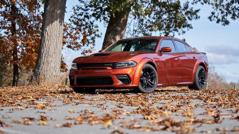 Orange Dodge Charger SRT Hellcat Widebody on a road covered in autumn leaves with trees behind.