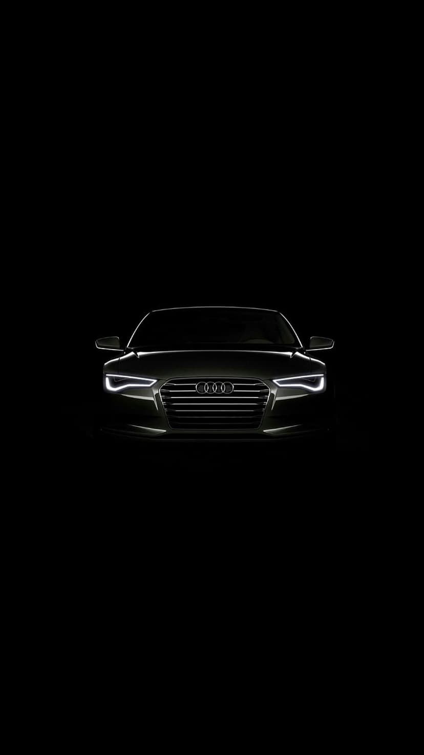 Audi car front grille and illuminated LED headlights glow against a solid black background in low light.