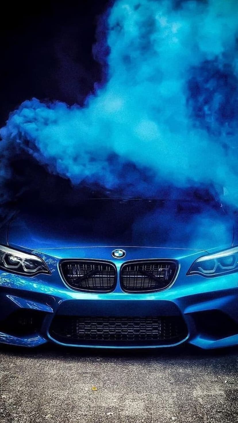 Blue BMW M2 sports car front grille and headlights partially hidden by thick swirling azure smoke clouds.