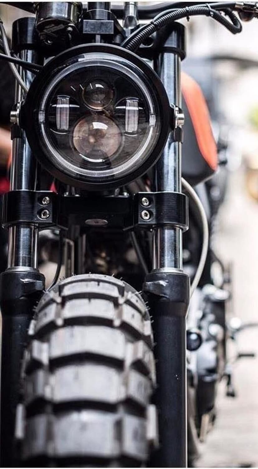 Vintage motorcycle LED headlight and knobby off-road tire with chrome forks and a shallow depth of field.