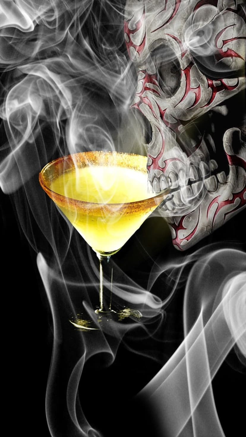 Skull-shaped smoke rises behind a yellow martini glass with a salted rim and red tribal markings on dark backdrop.