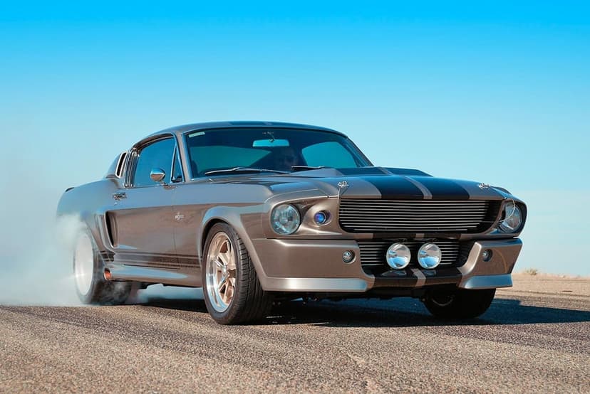 Silver Ford Mustang Shelby GT500 with black stripes performing a smoky tire burnout on an asphalt road.