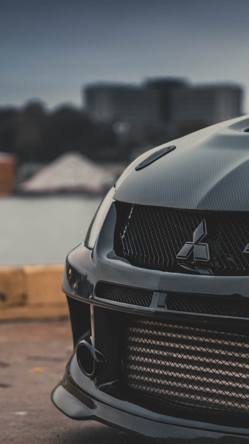 Black Mitsubishi Lancer Evolution front grille and carbon fiber hood in a moody, industrial setting.