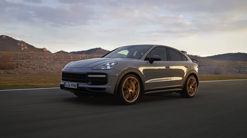 Grey Porsche Cayenne Coupe driving on a road at dusk with bronze wheels and a mountain landscape background.