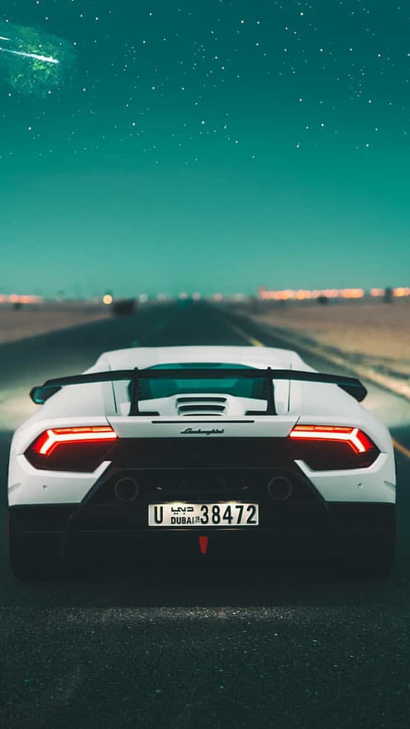 White Lamborghini Huracan with glowing red taillights driving on a dark Dubai road under a starry turquoise sky.