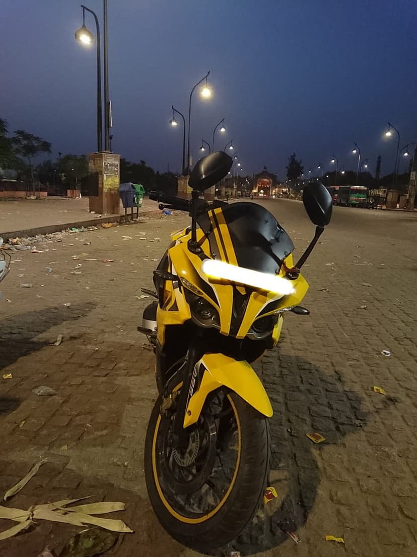 Yellow sport motorcycle with glowing headlights on a cobblestone street at night under warm urban lamps.