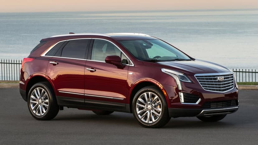 Maroon Cadillac XT5 luxury SUV parked on a coastal road overlooking a calm ocean at sunset with warm lighting.