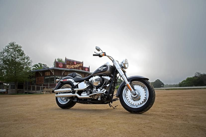 Harley-Davidson Fat Boy motorcycle with chrome wheels parked on dirt in front of a rustic wooden roadhouse.