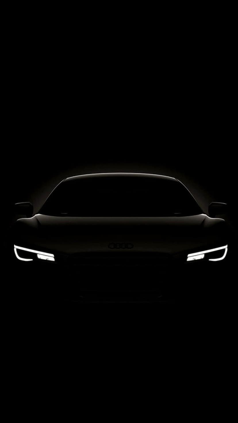 Audi R8 front end with glowing white LED headlights and a silver logo set against a solid black background.