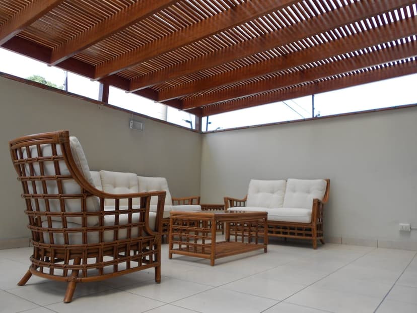 White wicker sofa and armchair sit on a tiled patio beneath a slatted wooden pergola in a modern garden setting.