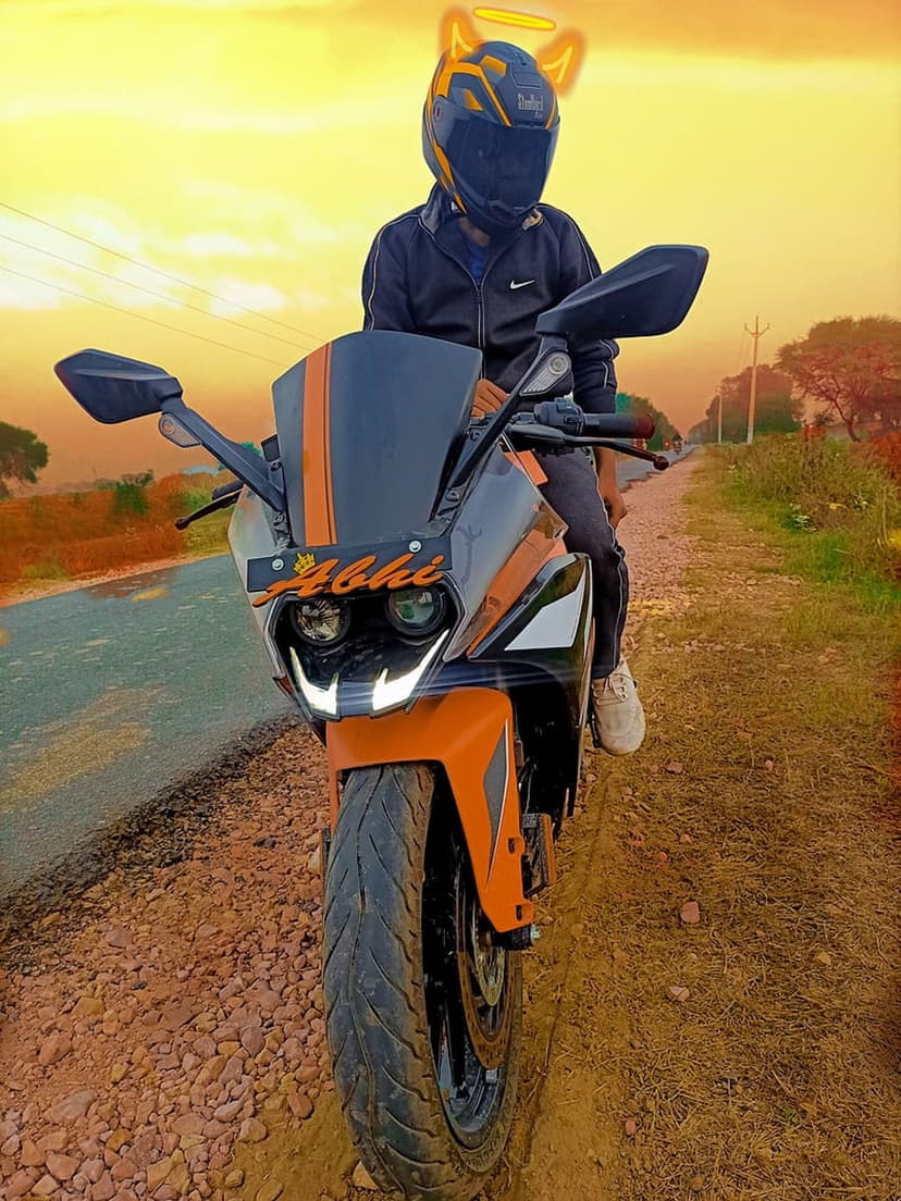 Biker wearing a cat-ear helmet poses on a vibrant orange sportbike while the setting sun creates a golden glow.